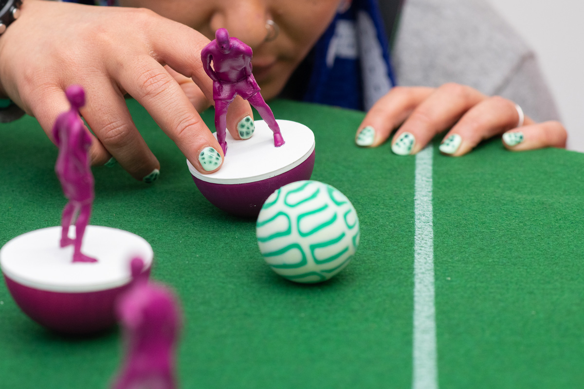 photo of hand playing with subbuteo style women and non-binary 3d printed footballers in purple on green felt