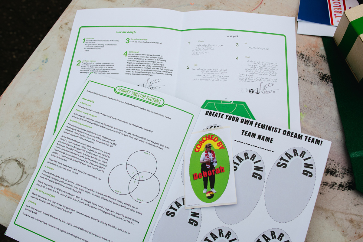 people playing feminist tabletop football with subbuteo-style women and non-binary 3d printed footballers on green felt