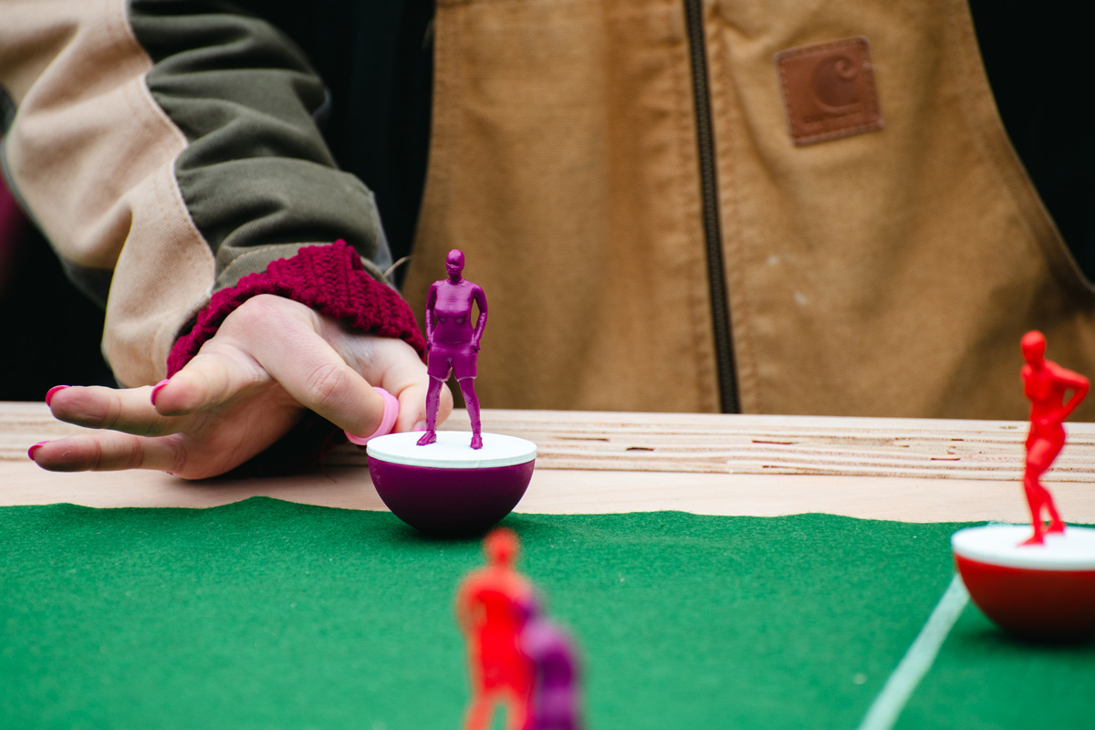 people playing feminist tabletop football with subbuteo-style women and non-binary 3d printed footballers on green felt