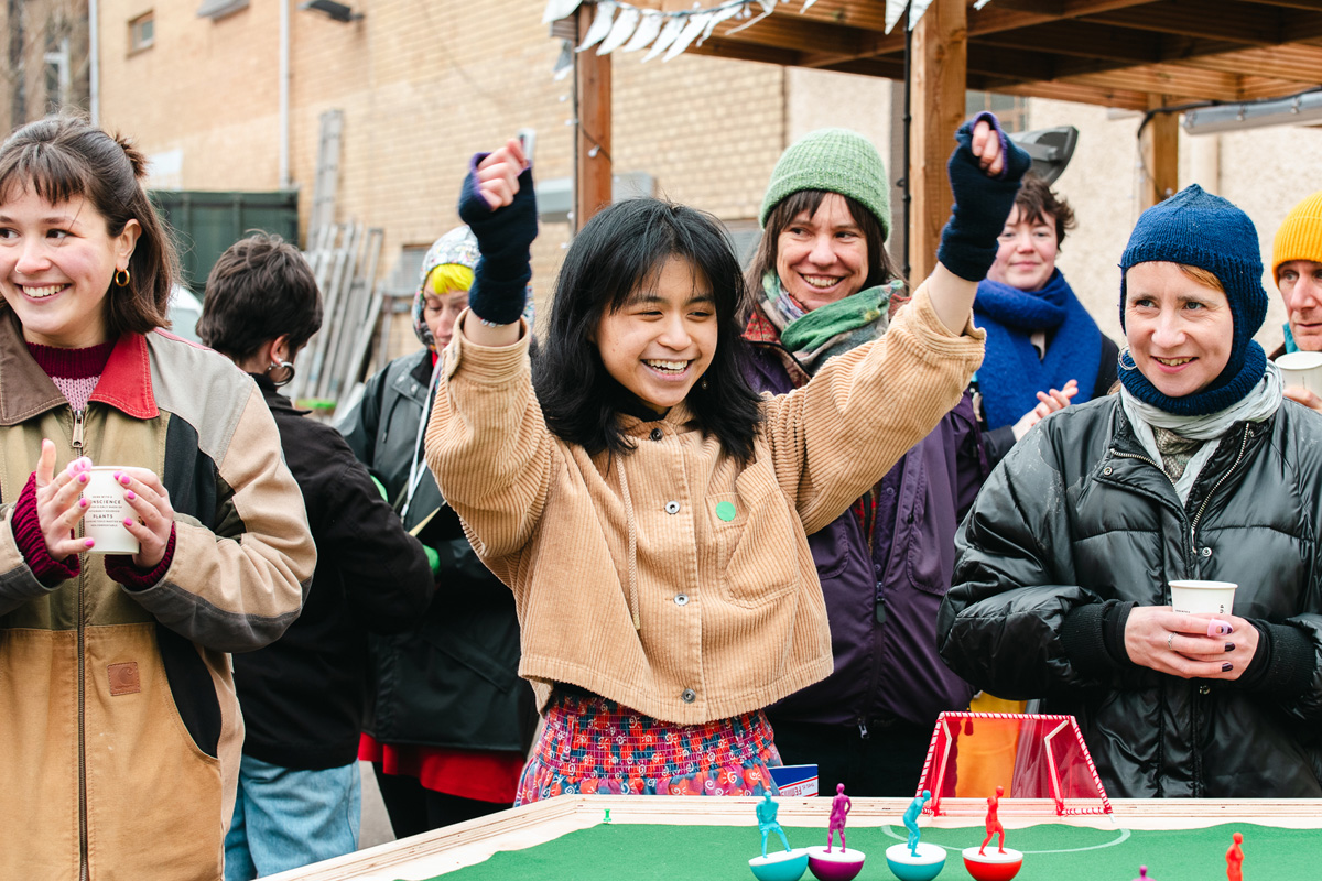 people playing feminist tabletop football with subbuteo-style women and non-binary 3d printed footballers on green felt