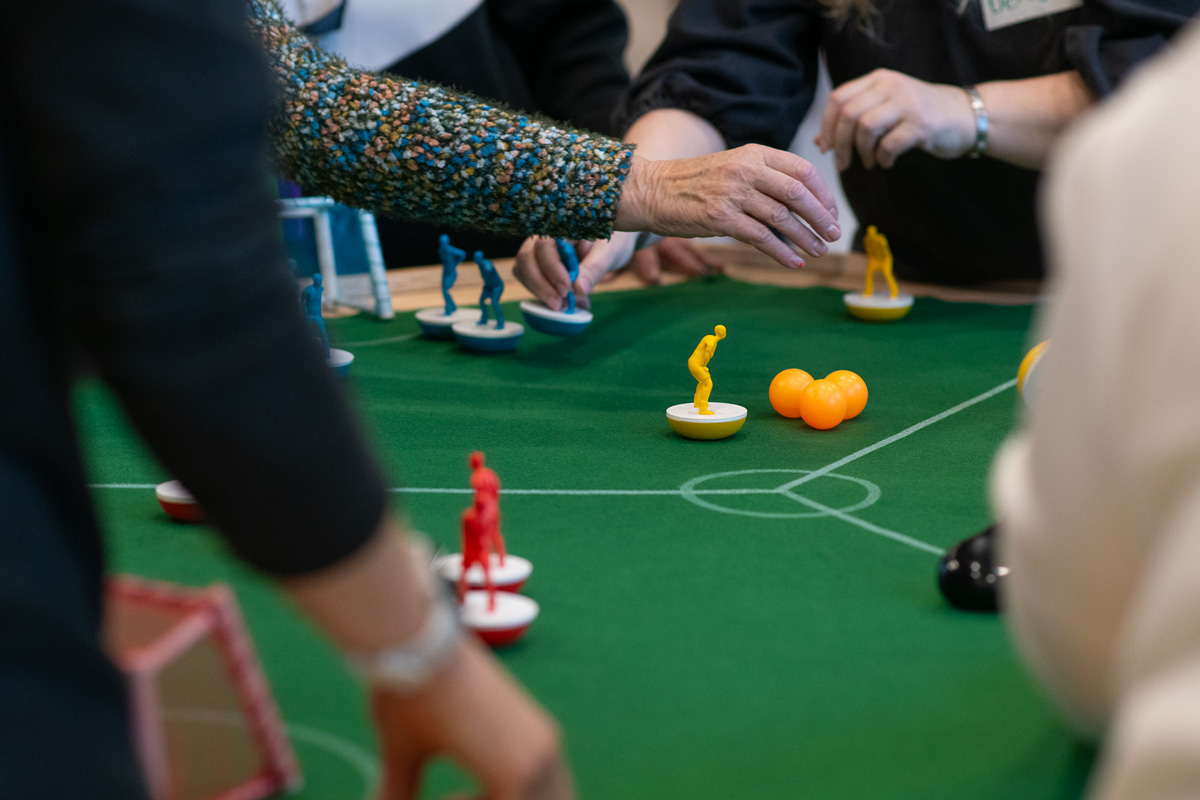 a group of older women playing feminist tabletop football with subbuteo-style women and non-binary 3d printed footballers on green felt