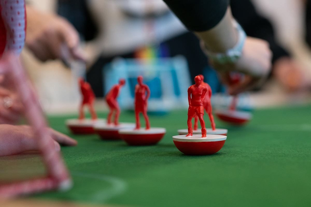 women playing feminist tabletop football with subbuteo-style women and non-binary 3d printed footballers on green felt